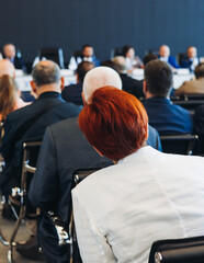 Obraz premium Audience at the modern conference hall listens to panel discussion, people on a congress event together listen to speaker on stage at convention, business seminar, large venue for forum presentation