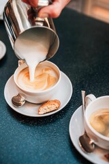 Barista pouring milk into cappuccino with biscotti