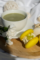 Green latte matcha with yellow and white sweet macaron on messy bed. Concept of holiday breakfast morning tea drink. Cozy minimalist superfood vibrant colors healthy eating. Organic caffeine-free