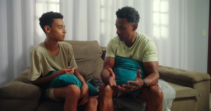 Father teaching life lessons to his teenage son, African descent family sharing a reflective moment of connection and understanding at home