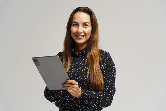 Smiling woman holding a tablet while wearing a polka dot blouse in a neutral studio setting - Powered by Adobe