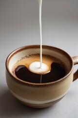 A stream of milk being poured into a cup of black coffee, creating a swirling pattern.