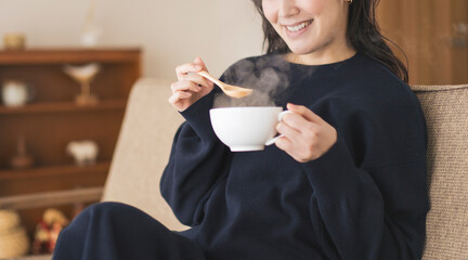 ソファーに座りカップスープを飲む女性。