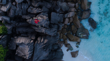 Drone view of model in red dress laying on beautiful rocks formation on Seychelles island