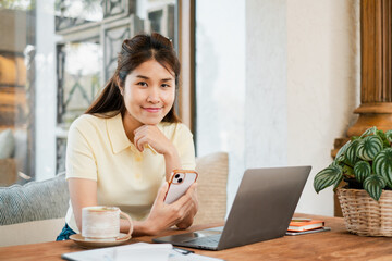Young woman enjoying coffee while working on a laptop and smartphone in a cozy cafe environment.