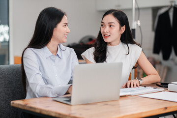 Two women engaged in a business discussion at a contemporary office, using a laptop and documents on a wooden table.