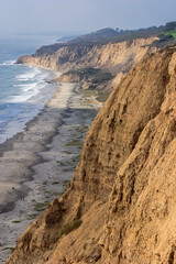 A rocky cliff overlooking the ocean with a few people walking on the beach