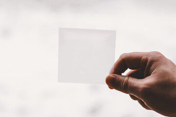 A man holds a Blank sticker in one hand, showcasing a minimalist design. The background is softly blurred, enhancing the object's simplicity in daylight. Place for your text