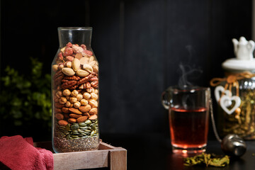 Mix of Nuts in a Beautiful Glass Vase with a Glass of Tea on the Background