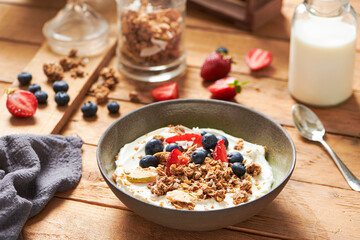 Healthy Breakfast with Glass of Milk and a Bowl with Fresh Granola, Muesli with Yogurt, Berries, Strawberries on a Wooden Table on Wooden background. Side View