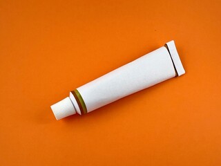 White tube commonly used for Pharmaceutical use of chemical product such as adhesives isolated on orange background