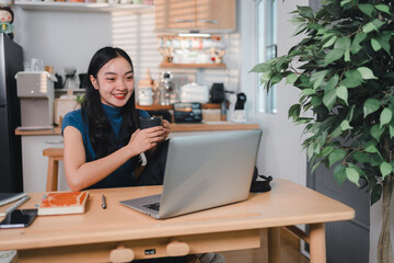 woman smiling while holding cup and working on laptop in cozy home office setting