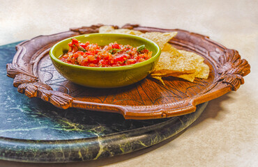 Fresh organic salsa in a vintage bowl and corn chips on an antique wooden plate on a marble tray.