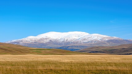 Fototapeta premium Snowy Mountains Under Clear Blue Sky with Distant Rolling Hills and Green Fields