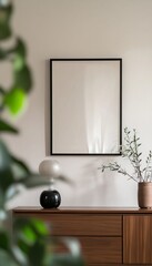Minimalist interior with blank frame, wooden dresser, lamp, and plants.