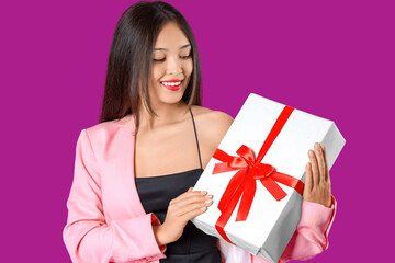 Beautiful young Asian woman with gift box on purple background
