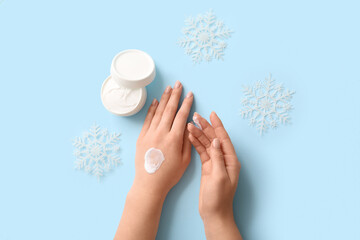 Woman applying cosmetic cream with snowflakes on blue background