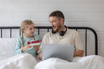 Obraz premium Father and daughter enjoy a joyful morning together as she surprises him with a gift in their cozy bedroom