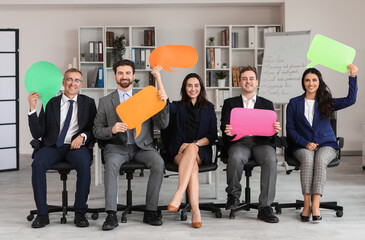 Team of business people with blank speech bubbles sitting in office