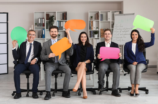 Team of business people with blank speech bubbles sitting in office