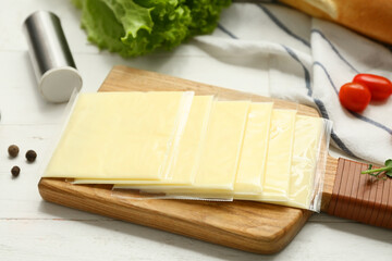 Board with slices of delicious processed cheese and fresh vegetables on white wooden table
