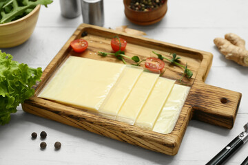 Board with slices of delicious processed cheese and fresh vegetables  on white wooden table