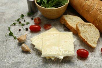 Slices of delicious processed cheese, fresh vegetables and bread on grey grunge table