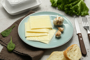 Plate with slices of delicious processed cheese, garlic and lettuce on grey grunge table
