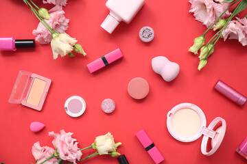Composition with bottle of perfume, makeup products, nail polish and flowers on red background