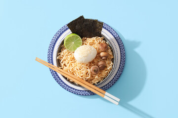 Bowl of tasty Chinese noodles with boiled egg, mushrooms and seaweed sheets on color background