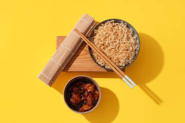 Bowls with tasty instant noodles, chopsticks and bamboo mat on yellow background