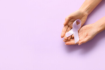 Woman holding lilac awareness ribbon on color background, top view. World Cancer Day