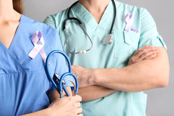 Doctors with lilac awareness ribbons on grey background, closeup. World Cancer Day
