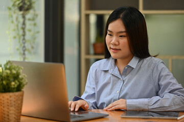 Fototapeta premium A professional woman engaged in remote work focused on her laptop, set against a modern office