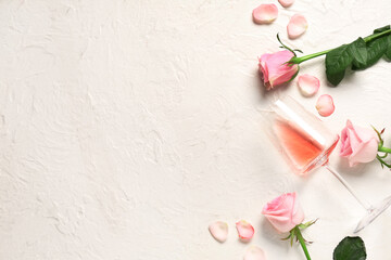 Glass of pink wine with beautiful roses and petals on white background