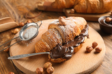 Board of sweet croissant with chocolate spread and hazelnuts on wooden background