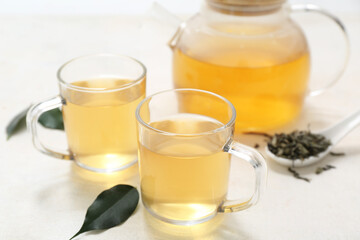 Glass cups and teapot of hot green tea with dried leaves on white background, closeup