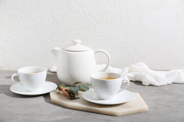 Cups and teapot of hot green tea with dried leaves on grey table