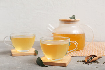 Glass cups and teapot of hot green tea with dried leaves on grey table