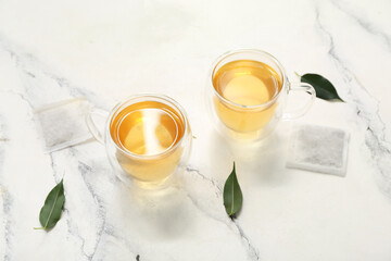 Glass cups of hot green tea and leaves on white background