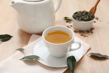 Cup and teapot of hot green tea with dried leaves on wooden background