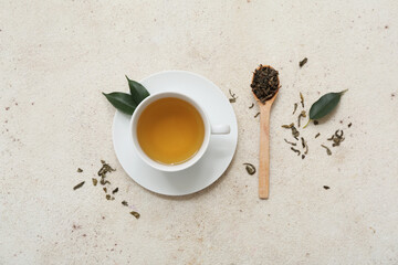 Cup of hot green tea and wooden spoon with dried leaves on white background