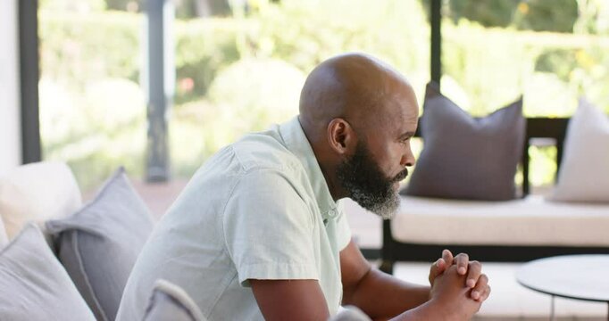 Man sitting on sofa, deep in thought, hands clasped together