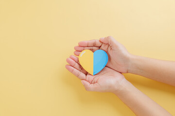 Yellow background with hands holding a divided yellow-blue heart marks Down Syndrome Day. Supporting Autism Awareness and raising Down Syndrome awareness