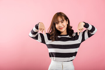 An Asian lady stands in a studio portrait, smiling and making a two-finger pointing gesture downwards. Isolated on pink, ideal for advertisements and promotions.