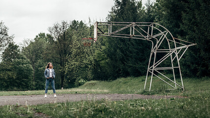 a woman standing by a basketball hoop, it is made of metal pipes and looks unusual.