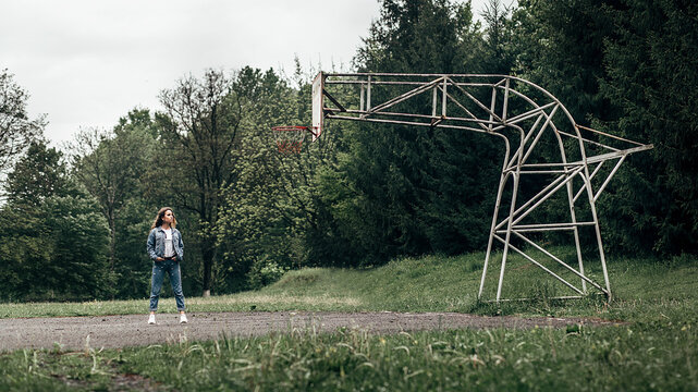 a woman standing by a basketball hoop, it is made of metal pipes and looks unusual.