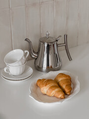 Breakfast is served with fresh croissants, a coffee pot, and cups on a bright table