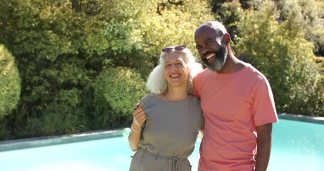 Smiling senior friends embracing and enjoying time together by swimming pool