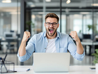 Man celebrating victory inside office at workplace, businessman working with laptop joyfully holding hands up, satisfied received excellent results achievement.